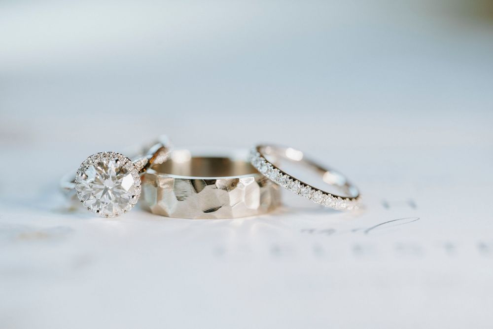 Three silver wedding rings including a diamond engagement ring, a hammered band, and a diamond eternity band on white paper.