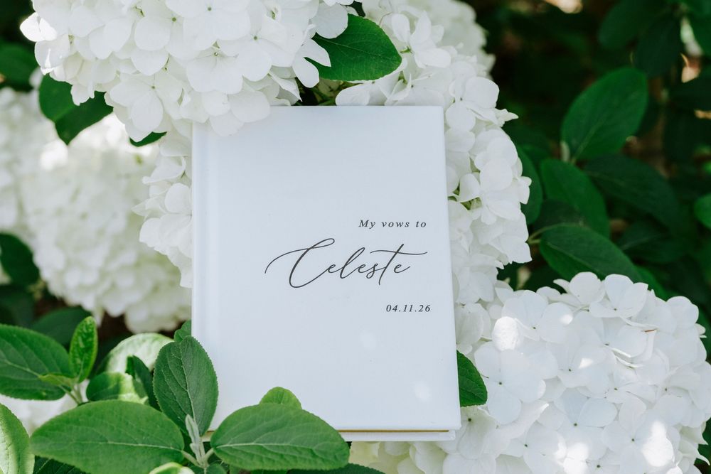 White vow book personalized for Celeste surrounded by blooming white hydrangea flowers.
