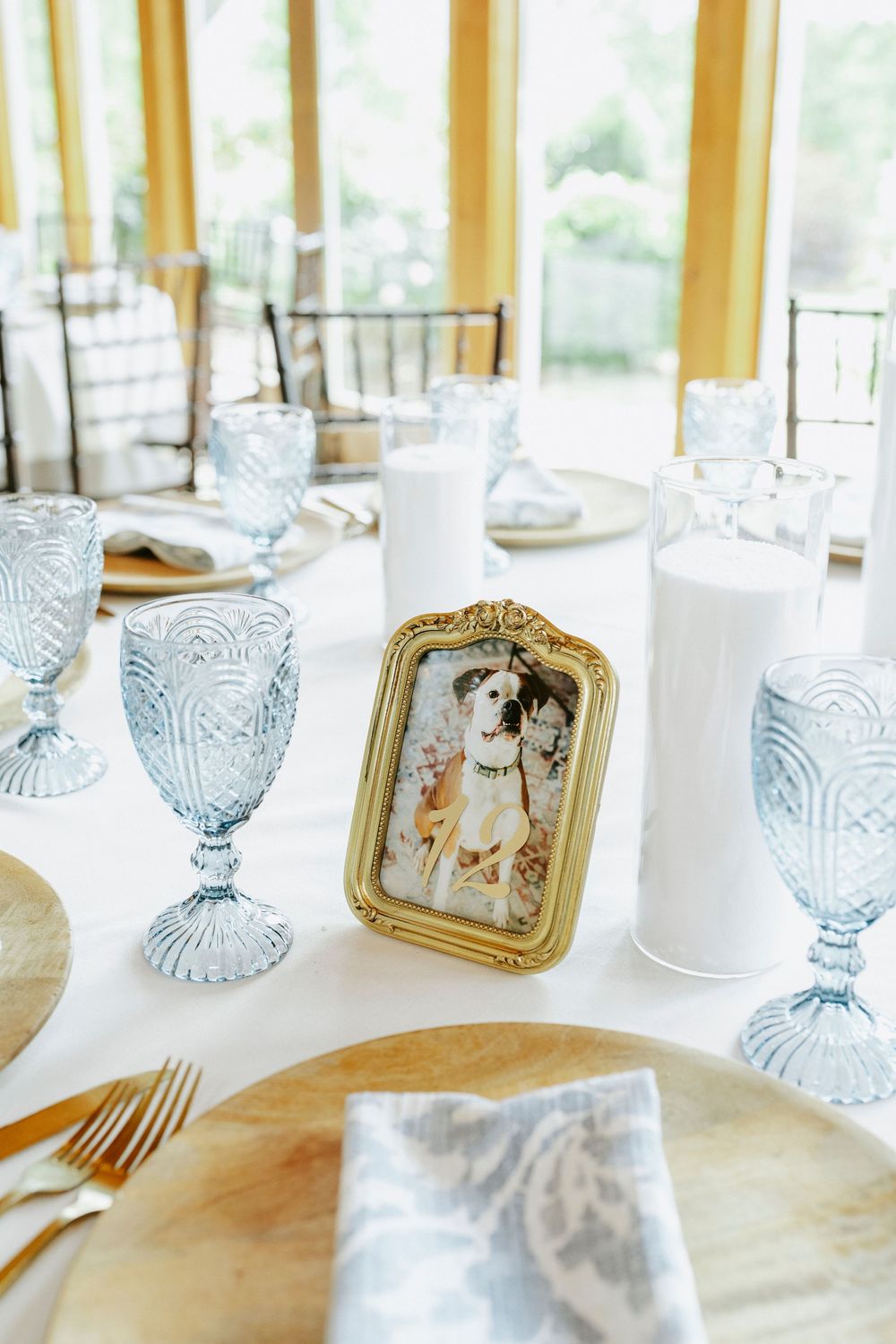 Elegant wedding table setting with blue goblets, gold frames, white candles, and a dog portrait centerpiece.