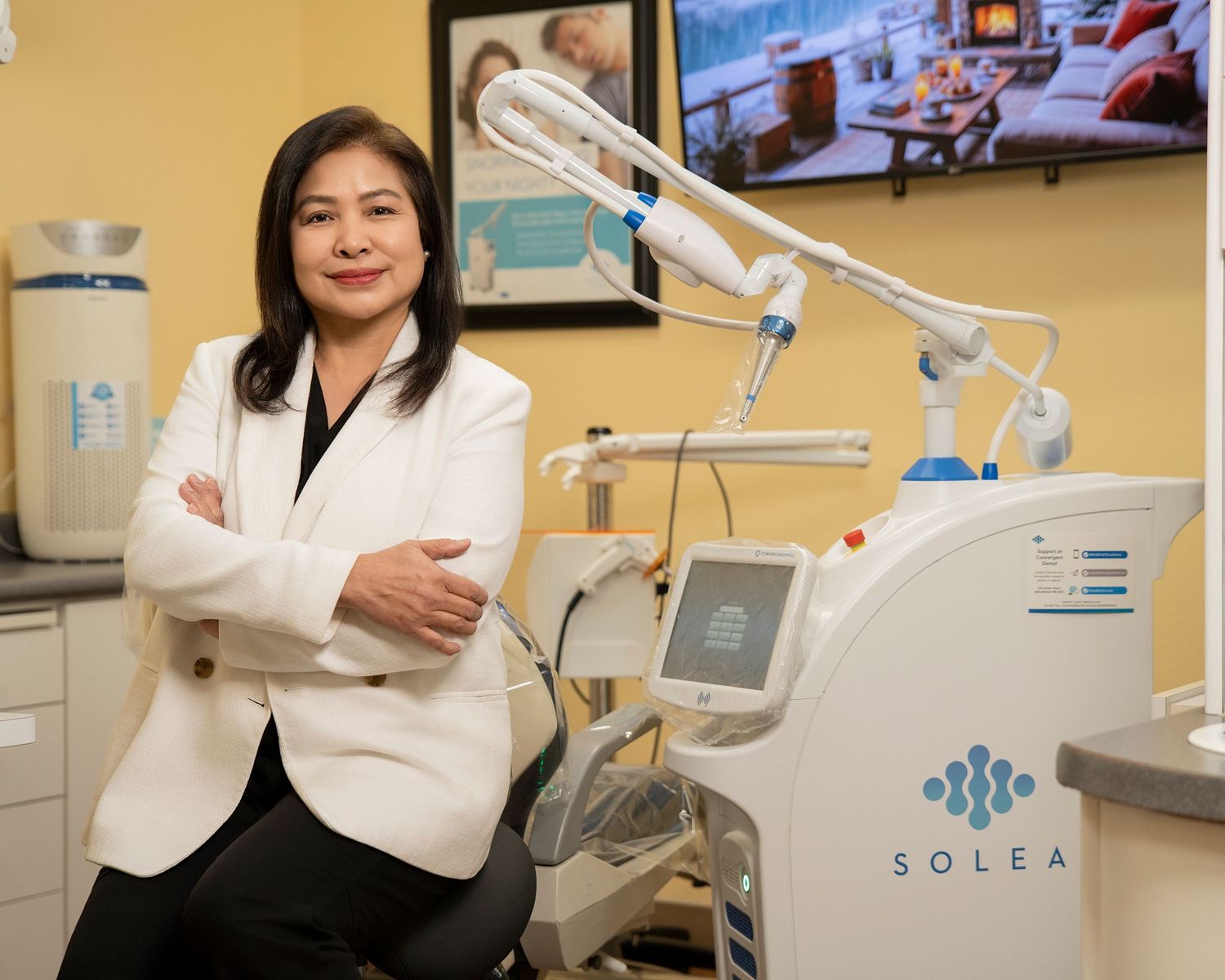 A smiling dental team of six professionals poses together in a modern dental office, wearing scrubs and white coats.