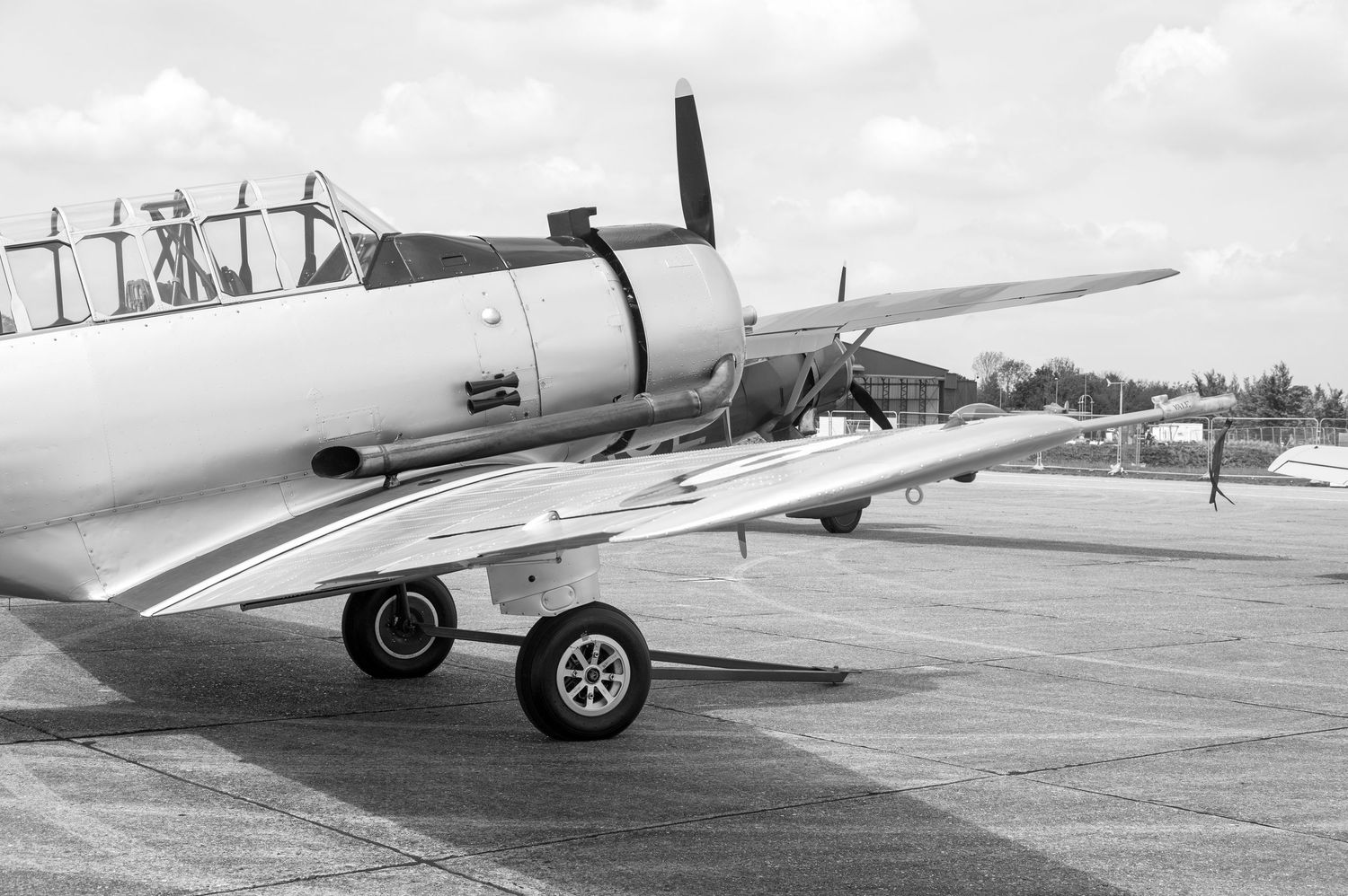 Vintage WWII-era propeller aircraft parked on tarmac, black and white photo showcasing wing detail and landing gear.
