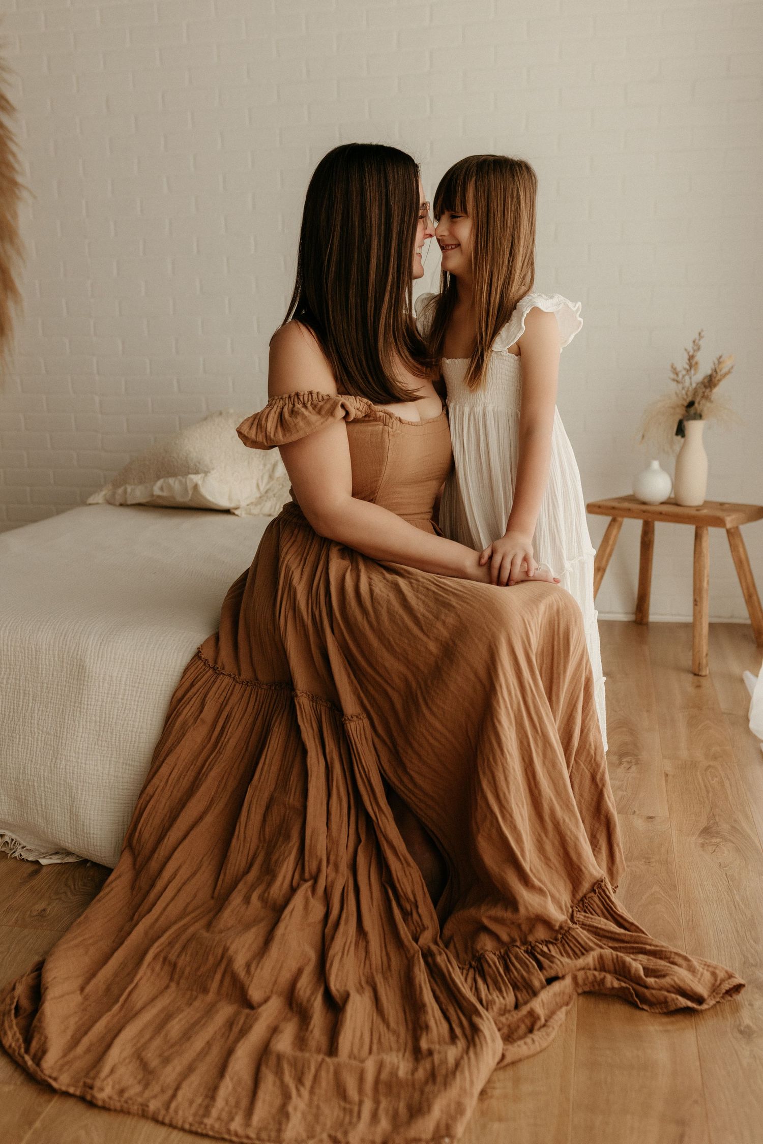 A mother and daughter share a tender moment, sitting together in a boho-styled room with warm earth tones.