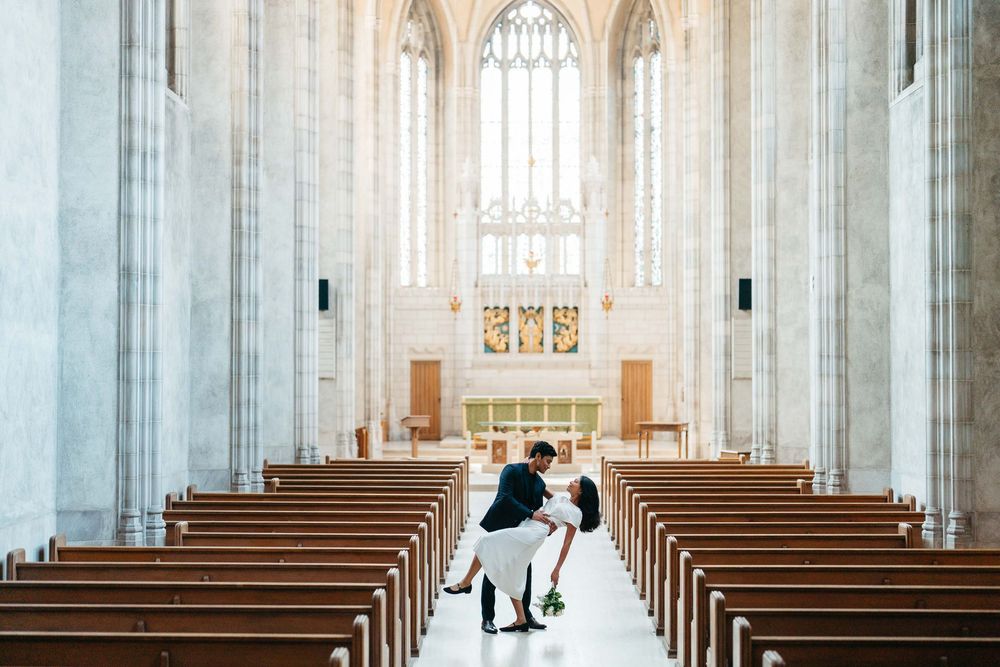 Bride and groom sharing romantic dip kiss in stunning Gothic cathedral with wooden pews and stained glass.