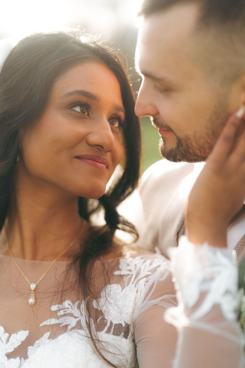 A bride and groom share an intimate moment, nearly touching foreheads, bathed in warm golden sunlight.