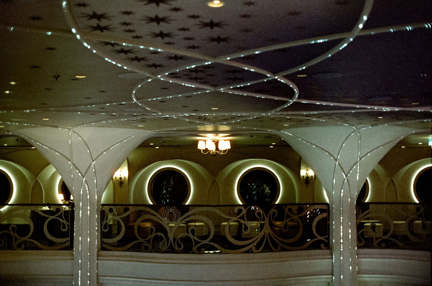 Elegant ballroom ceiling with swirling light strands, ornate white columns, and circular mirrors in a luxurious interior.