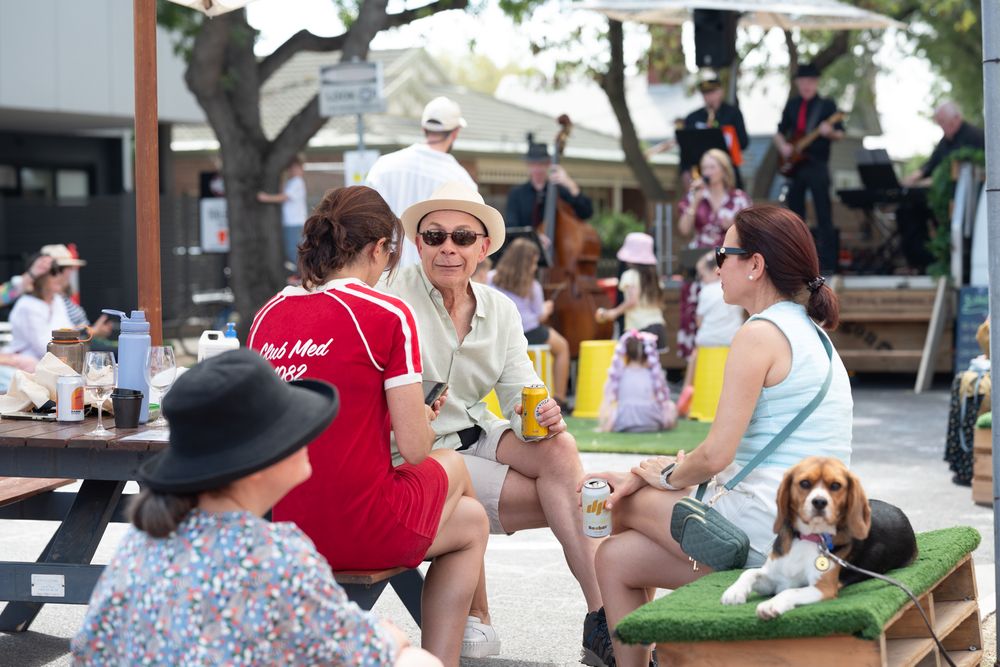 Group of women socializing at outdoor picnic tables with a beagle dog during a sunny community event.