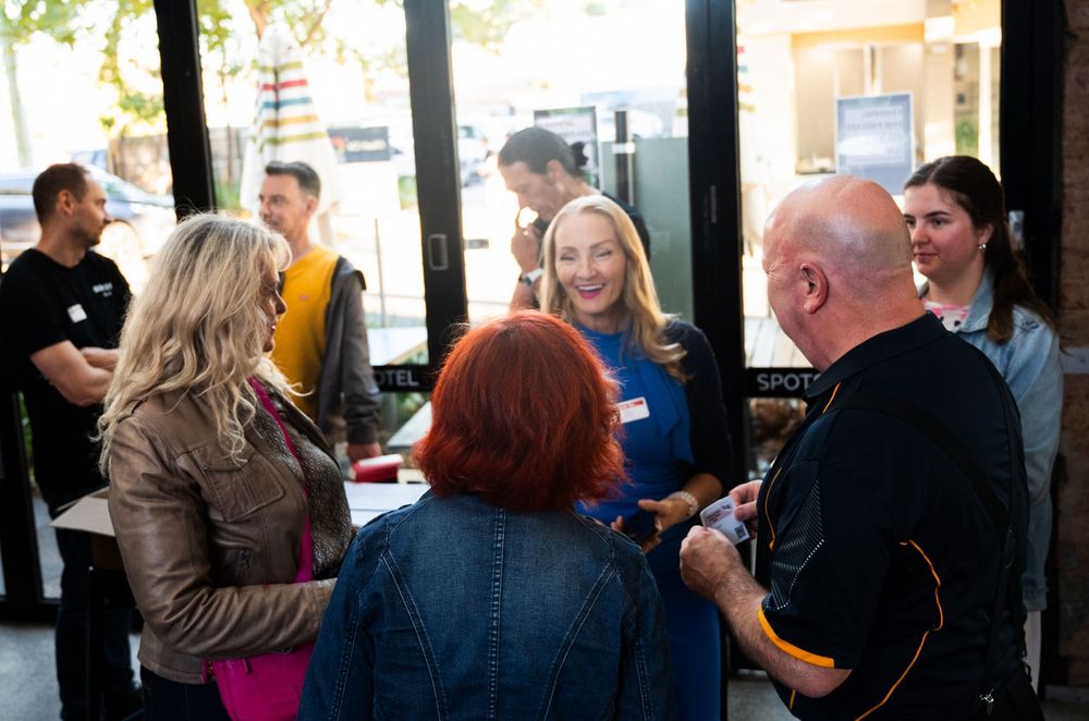 A group of smiling people networking and chatting outside a modern venue.