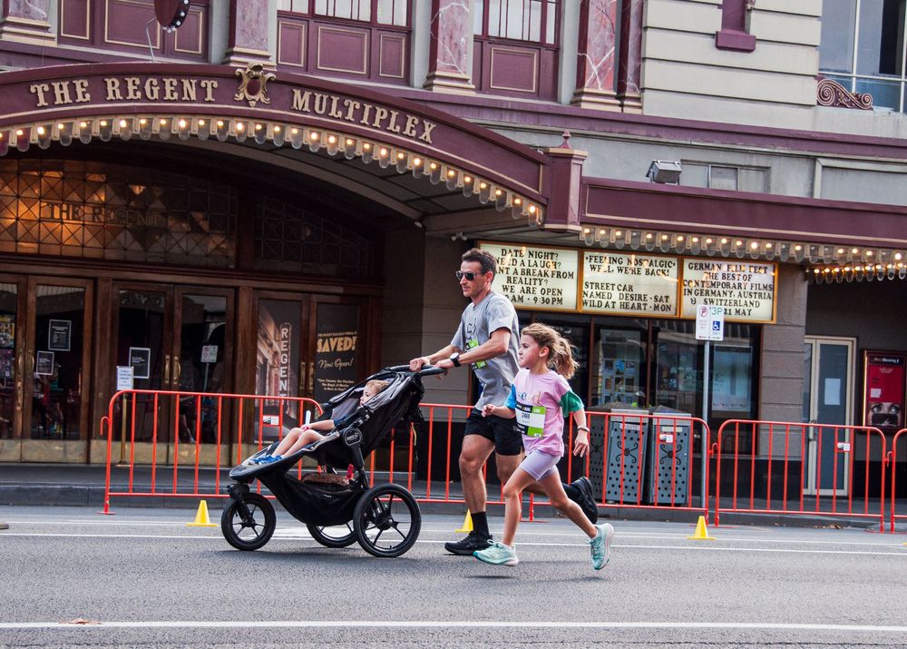 A man pushes a stroller while running with a child past The Regent Multiplex.