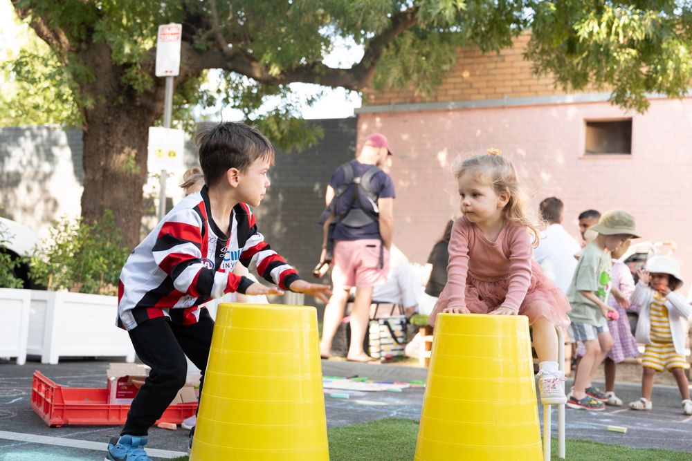 Two young children playing with large yellow cups outdoors during a fun school activity day.