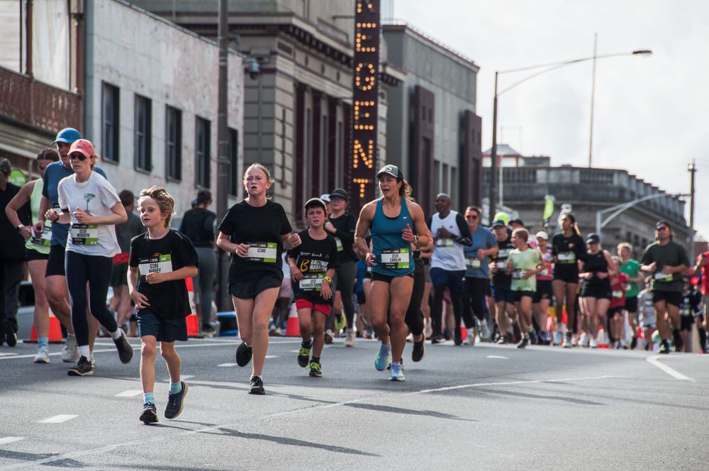 Runners race through a city street past a historic building in a marathon event.