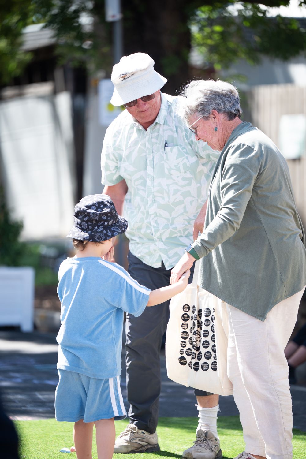 Grandparents and young child interacting outdoors on a sunny day at a community gathering.