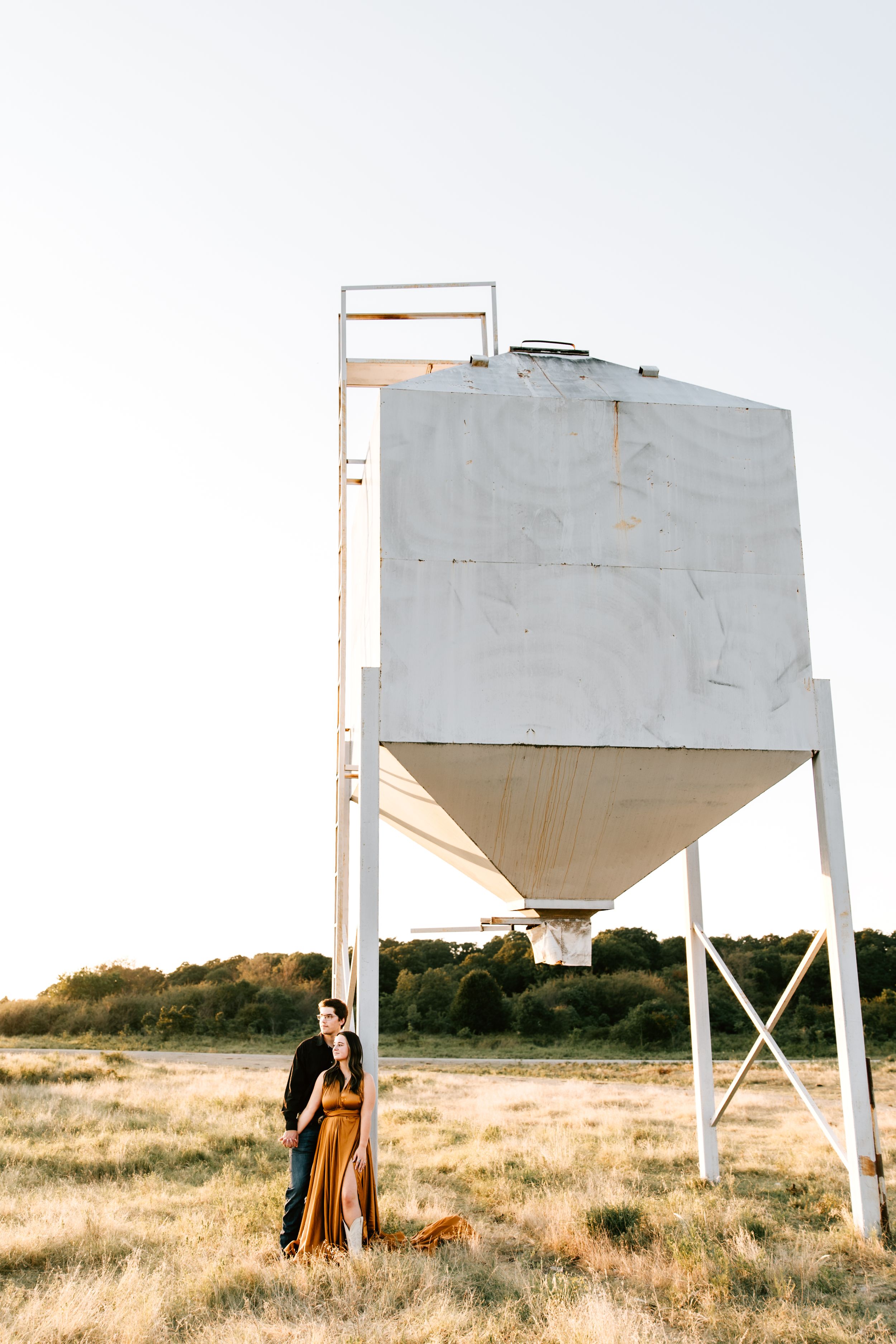 An engaged couple pose next to a cattle feed bin during their engagement session on their family ranch in Osage County Oklahoma.