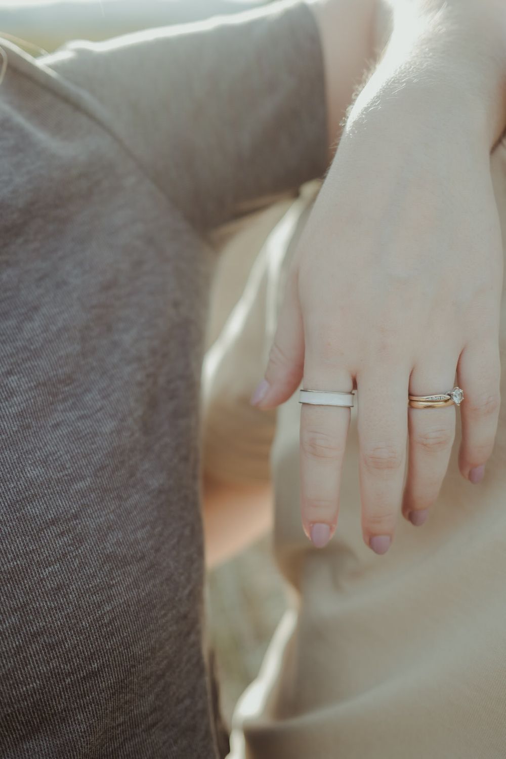 Close-up of couple holding hands showing wedding and engagement rings during an outdoor maternity photoshoot.