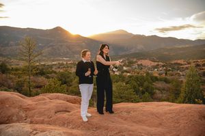 Two women stand on red rocks at sunset with mountain views at Garden of the Gods, Colorado.
