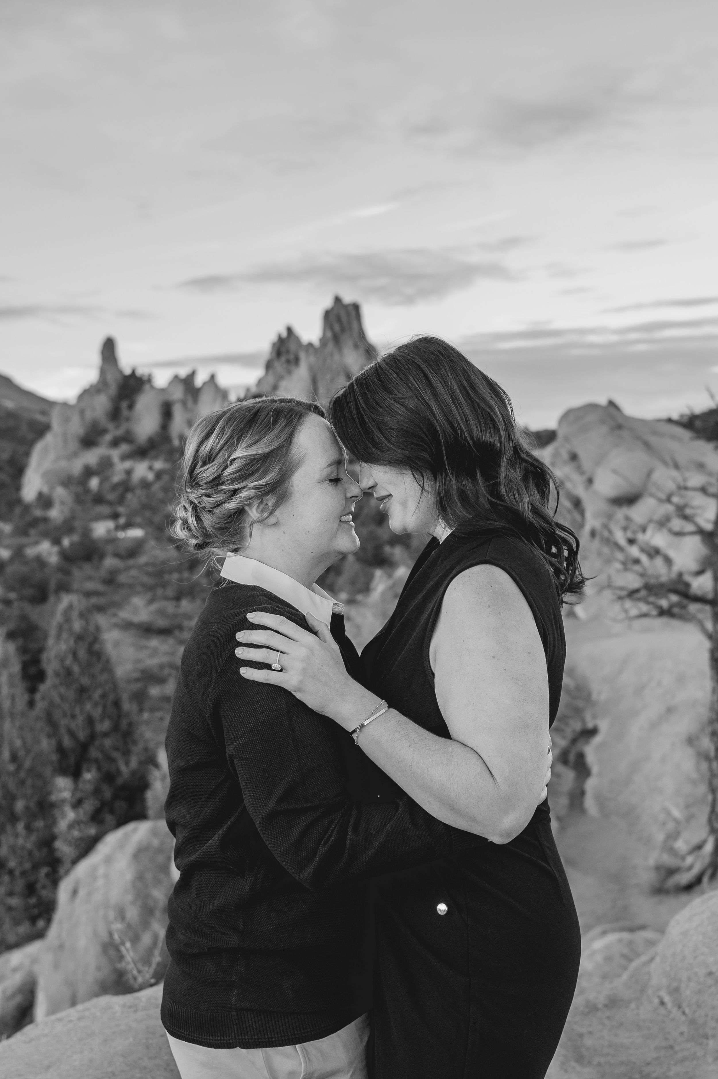 Black and white photo of two women embracing tenderly with dramatic rock formations in the background.