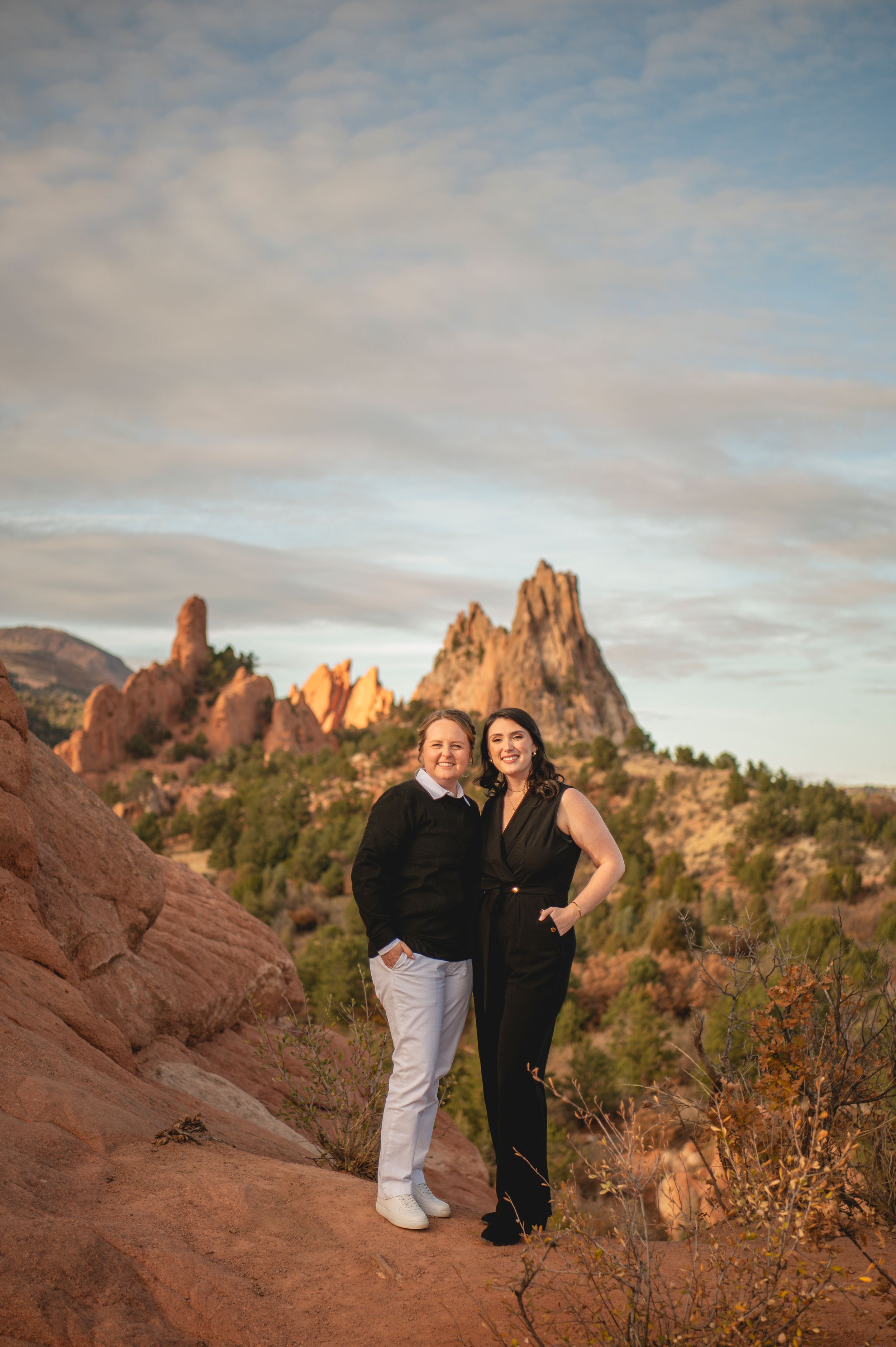 Two women smiling together at Garden of the Gods, Colorado, with red rock formations and blue sky backdrop.