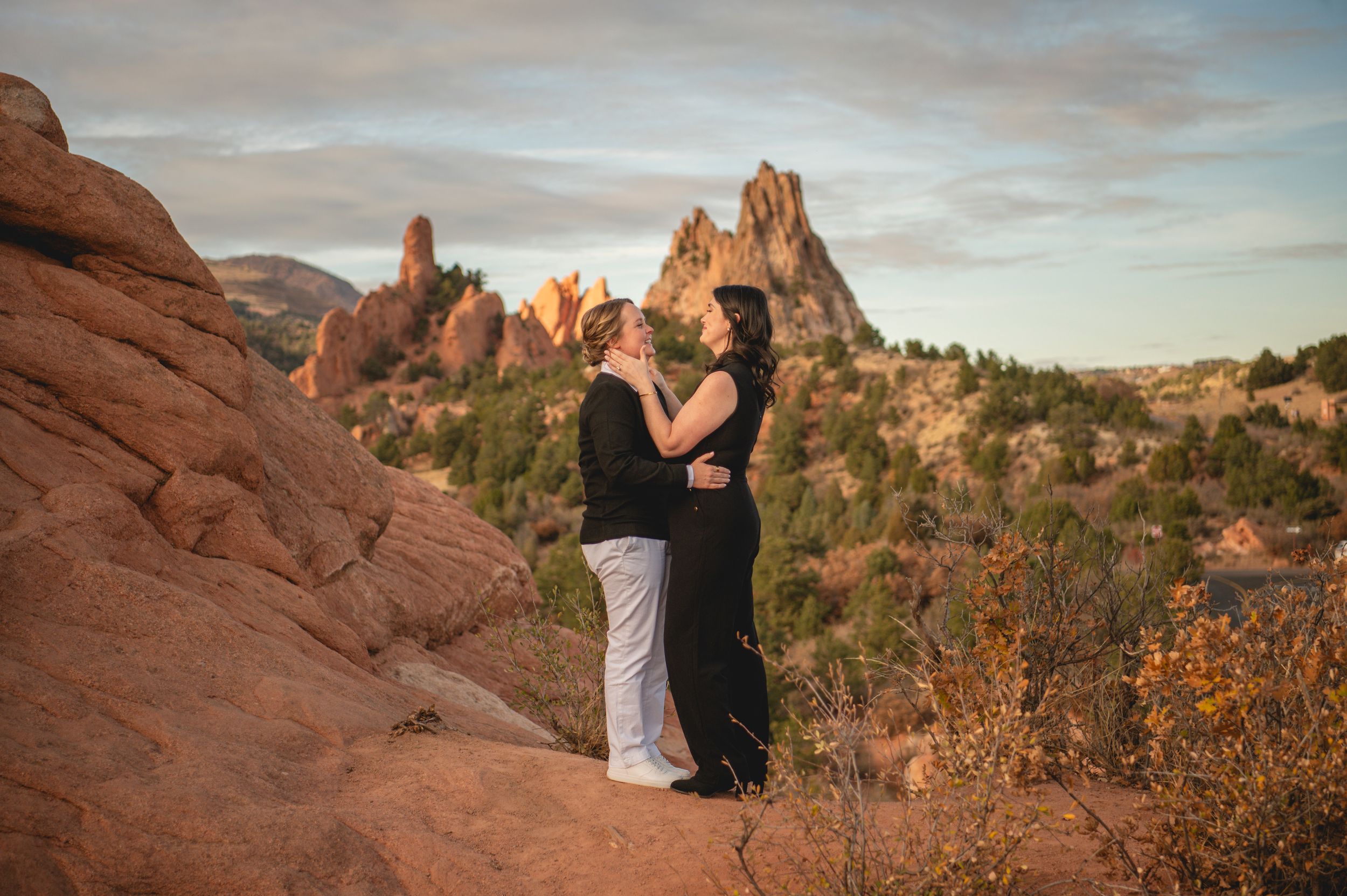 Couple embracing at Garden of the Gods, Colorado, with red rock formations at sunset.