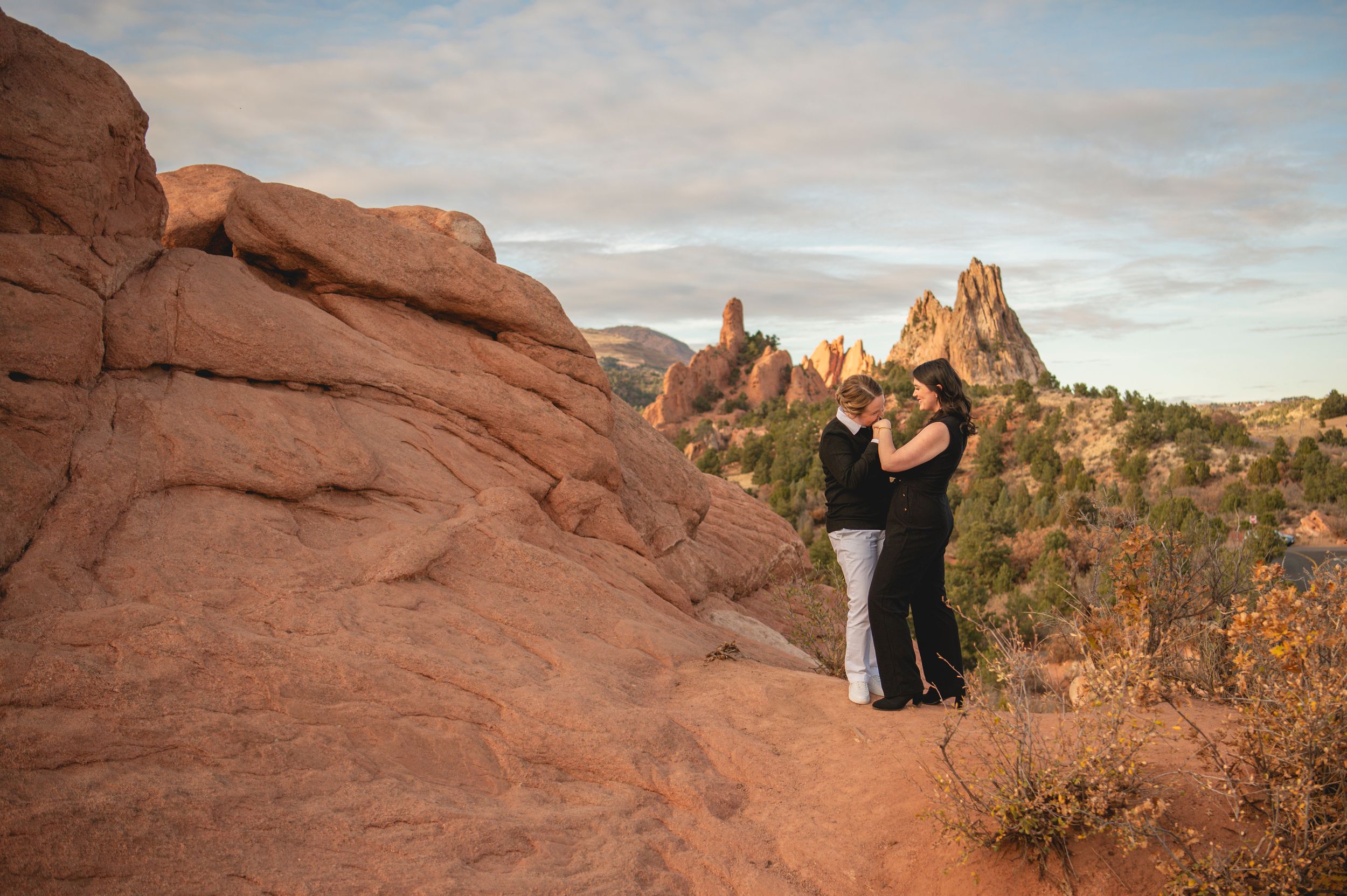 Couple embracing at Garden of the Gods, Colorado, surrounded by red rock formations at sunset.
