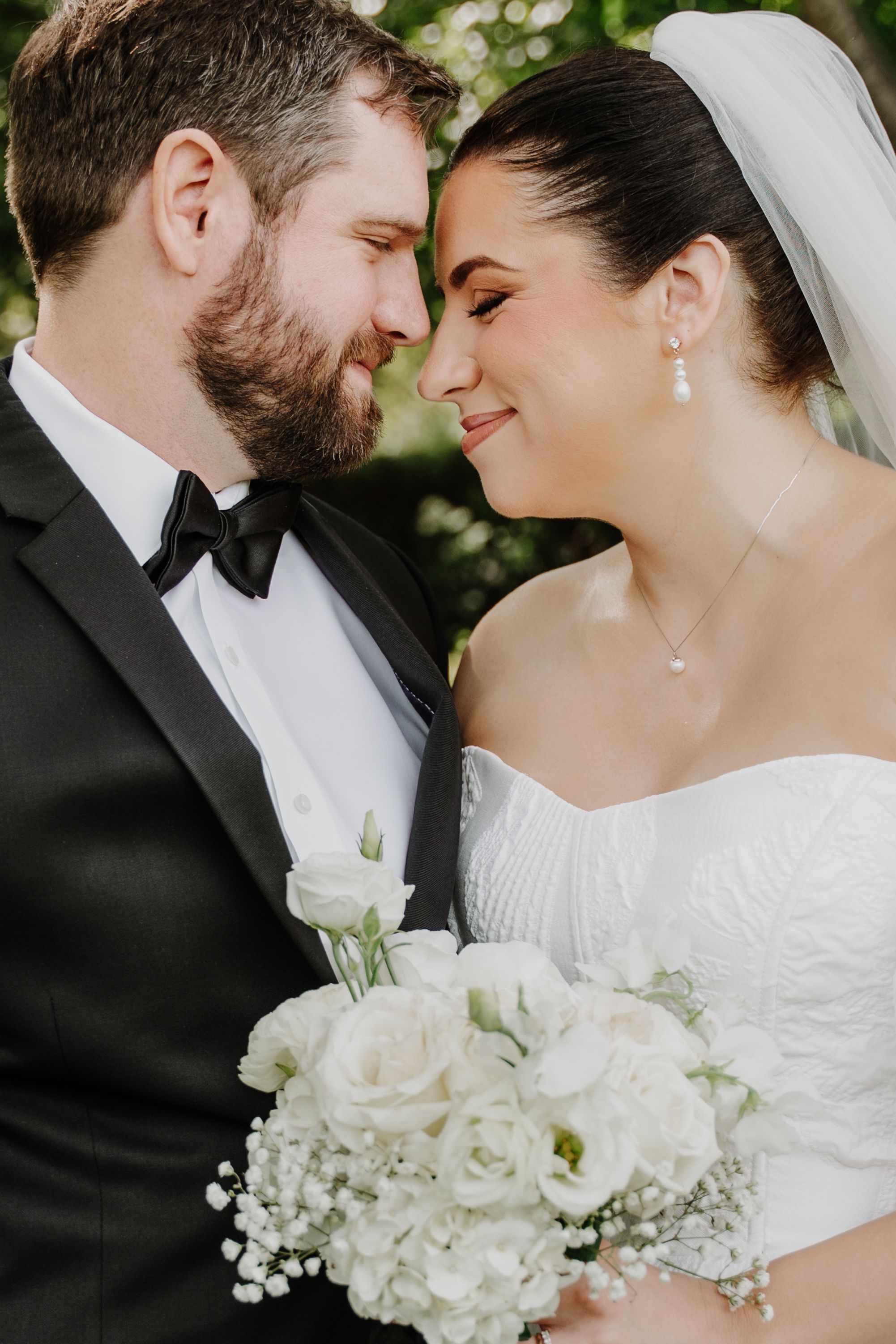 Bride and groom in elegant wedding attire share an intimate moment, bride holding white rose bouquet with baby's breath.