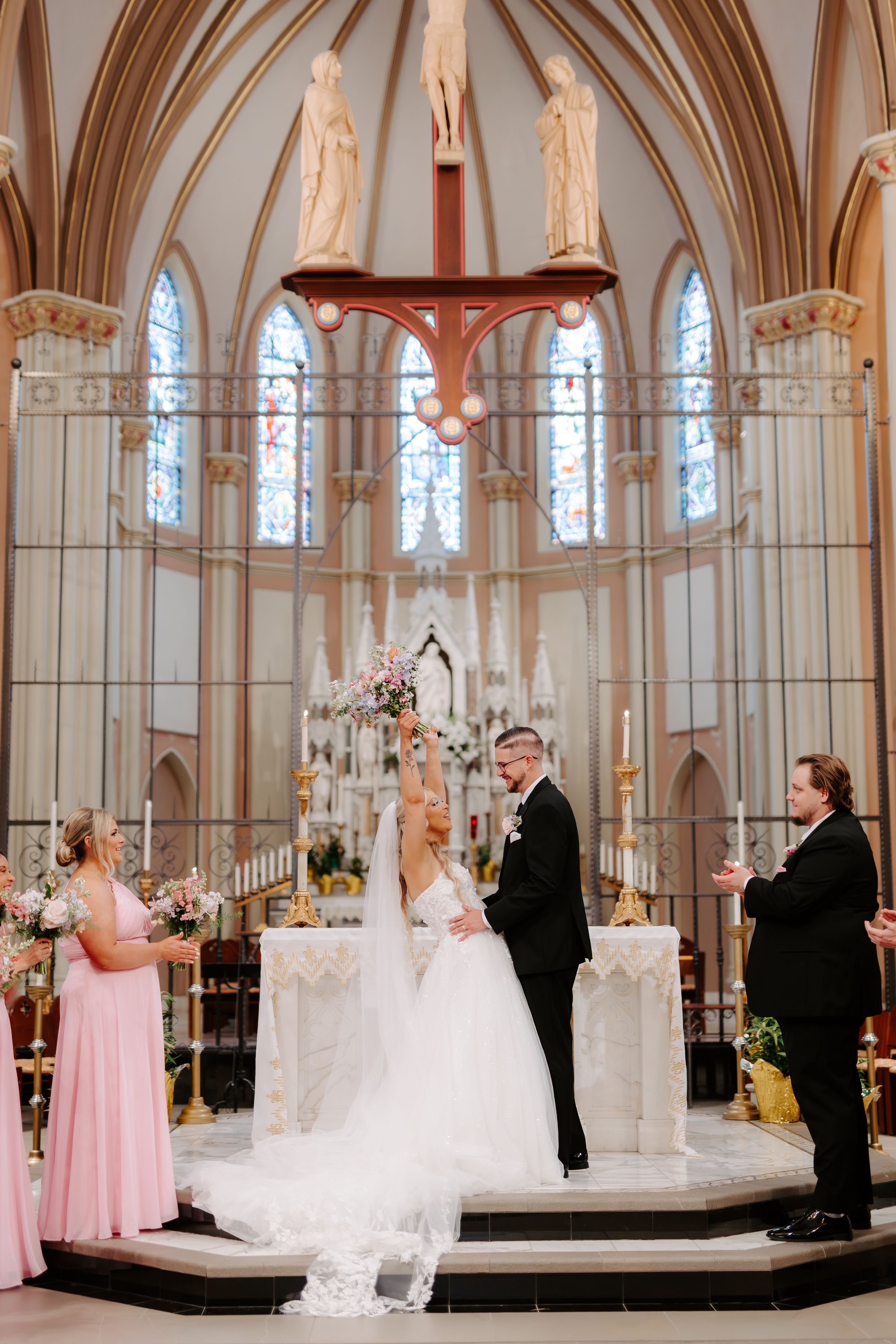 Bride and groom exchange vows at a stunning Gothic Catholic church altar, with bridesmaid and officiant nearby.
