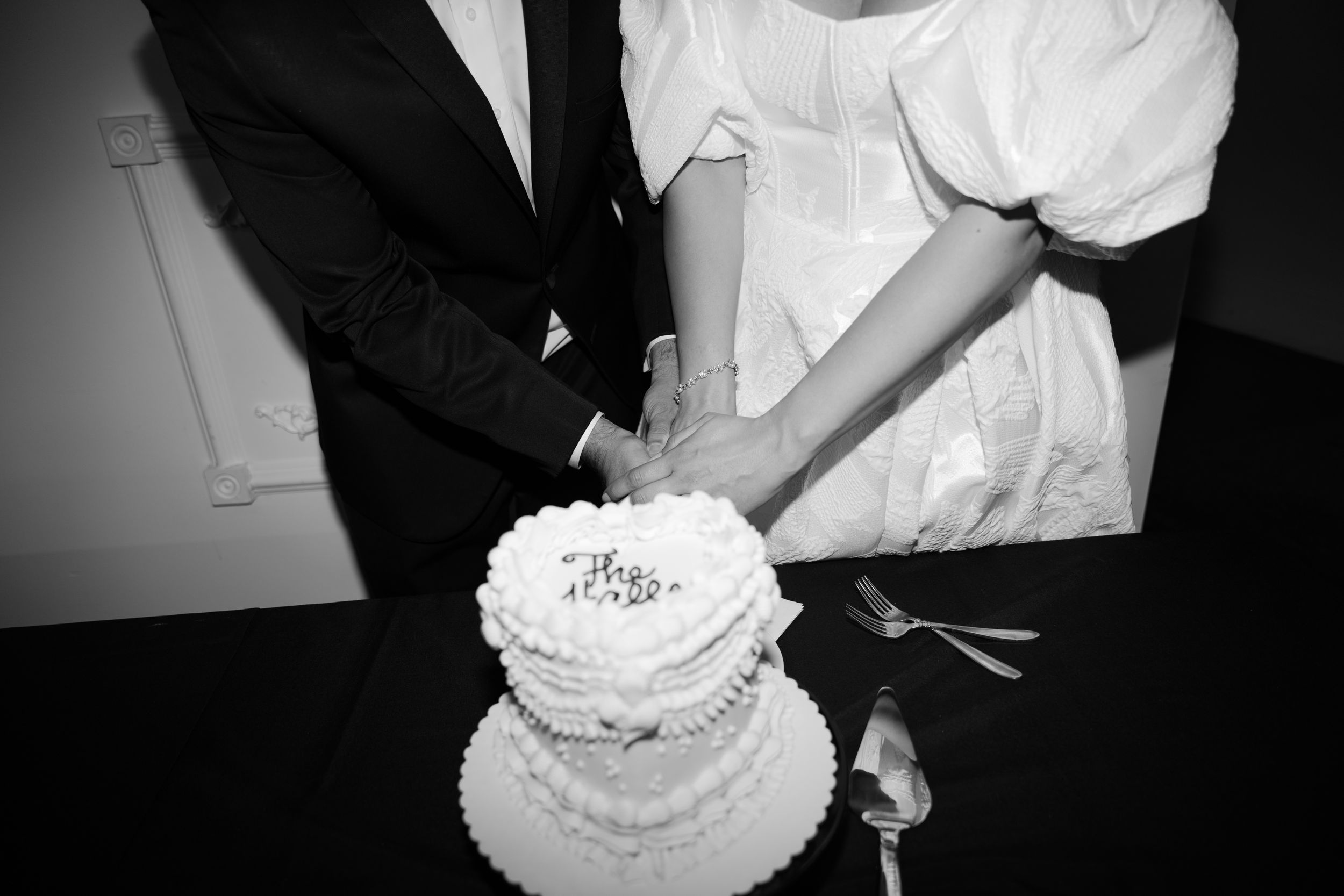 Bride and groom cutting white tiered wedding cake together in black and white photo.