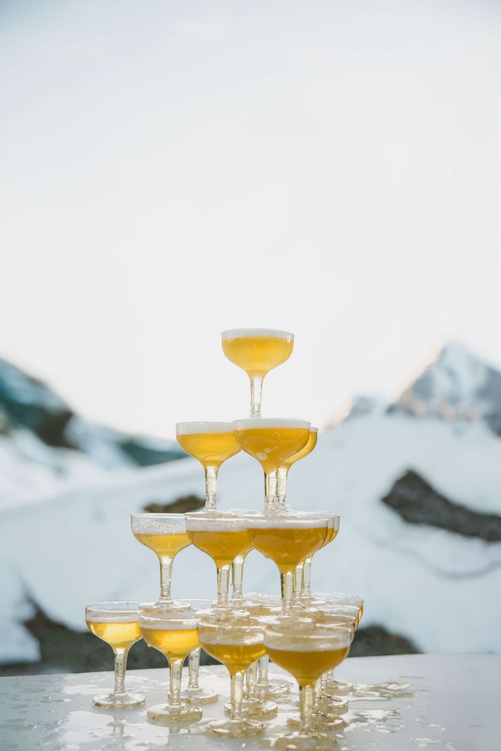 Elegant champagne tower pyramid with golden bubbly set against a snowy mountain backdrop at a winter wedding.