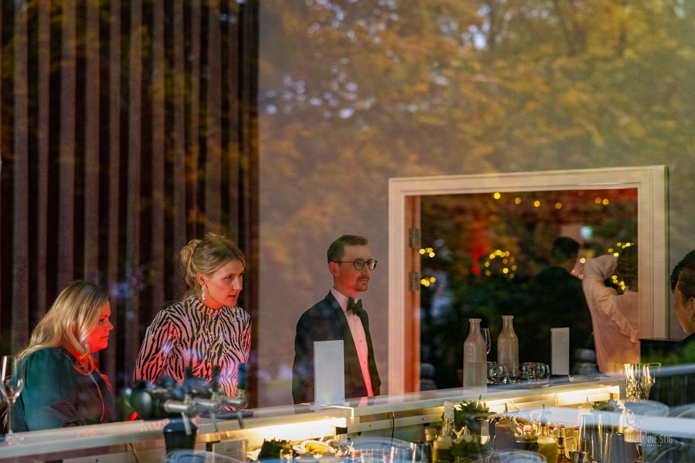 Elegantly dressed guests mingle at an upscale indoor event with warm ambient lighting and a decorated table.