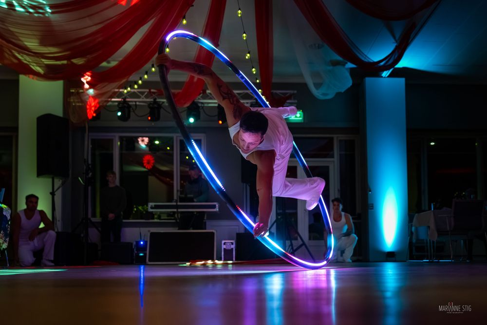 Performer balancing inside a glowing LED hula hoop on a dance floor at a colorful circus-themed event.