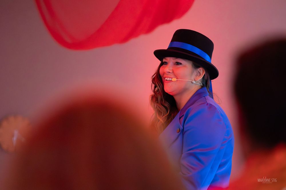 Smiling woman wearing a black hat with blue band performing under colorful stage lighting.