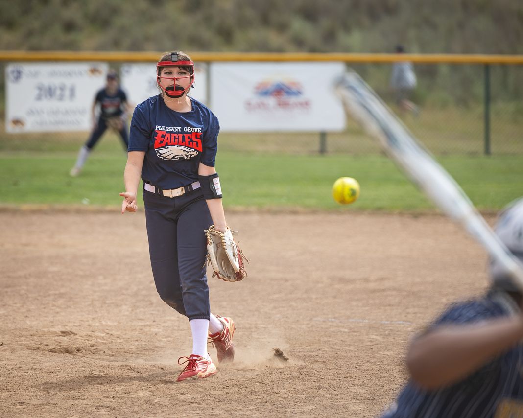 Softball pitcher in navy Eagles uniform mid-throw on dirt mound during competitive game.