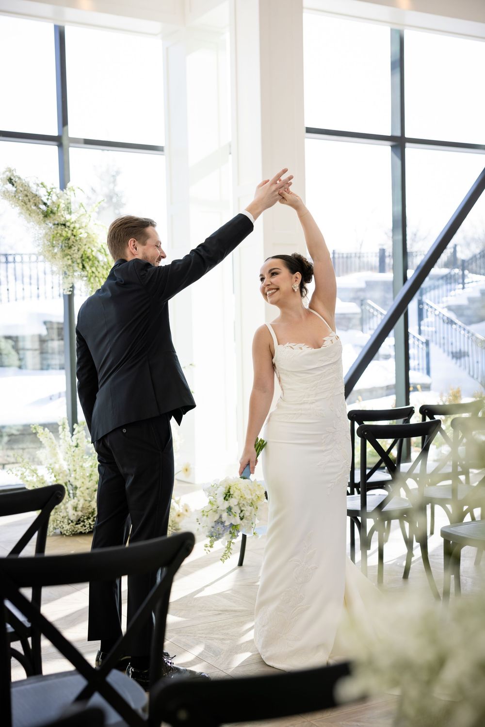 Groom twirling smiling bride in white gown during joyful wedding ceremony dance.