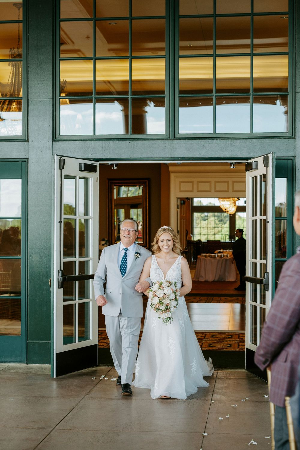Bride walks down the aisle with her father through elegant green French doors at a wedding venue.
