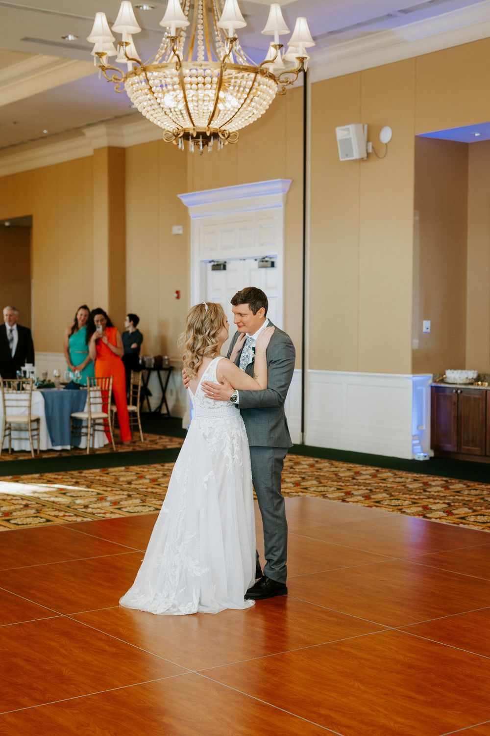 Bride and groom share their first dance under a crystal chandelier in an elegant ballroom wedding reception.
