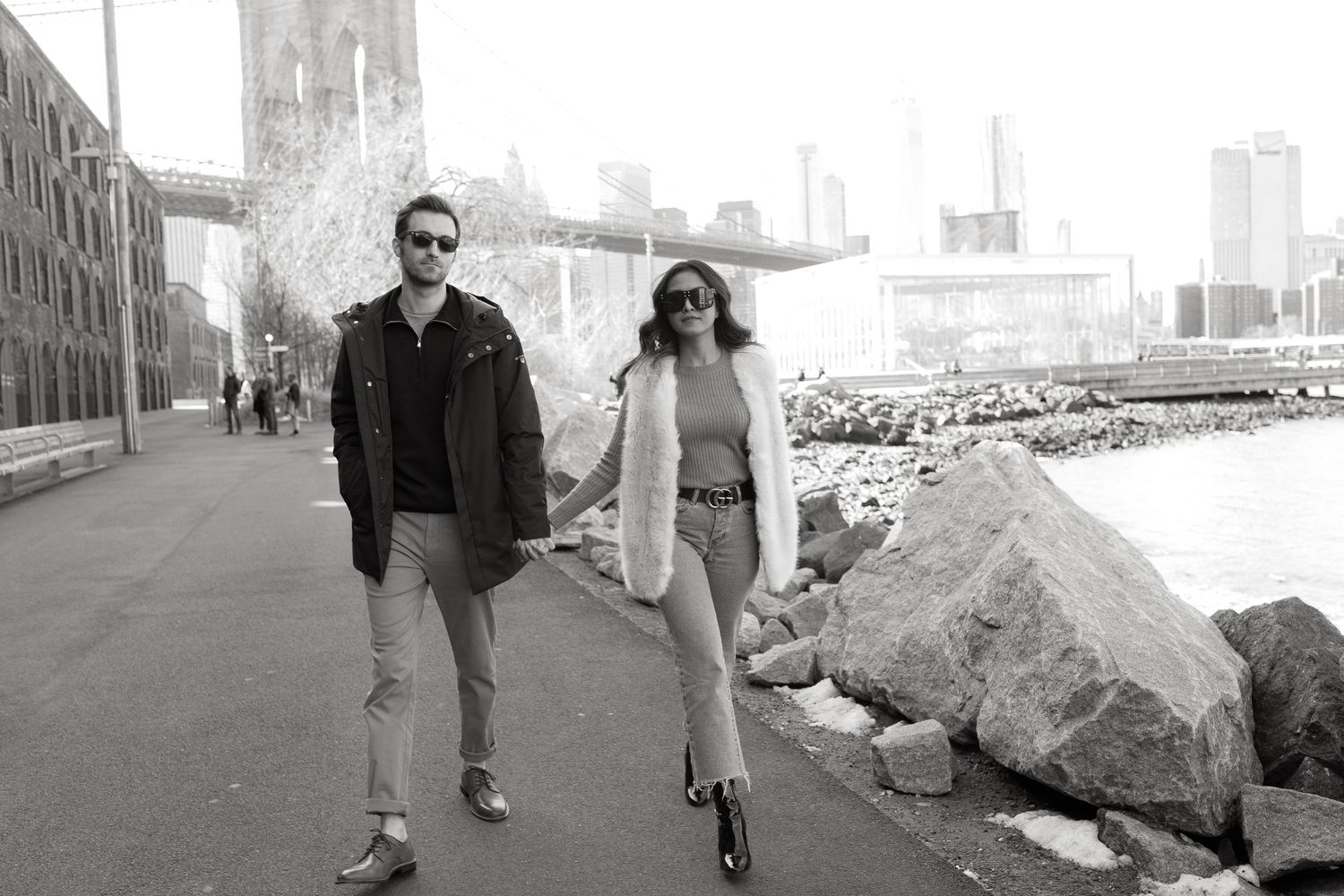 Casual couple walking across urban crosswalk with city buildings in background.