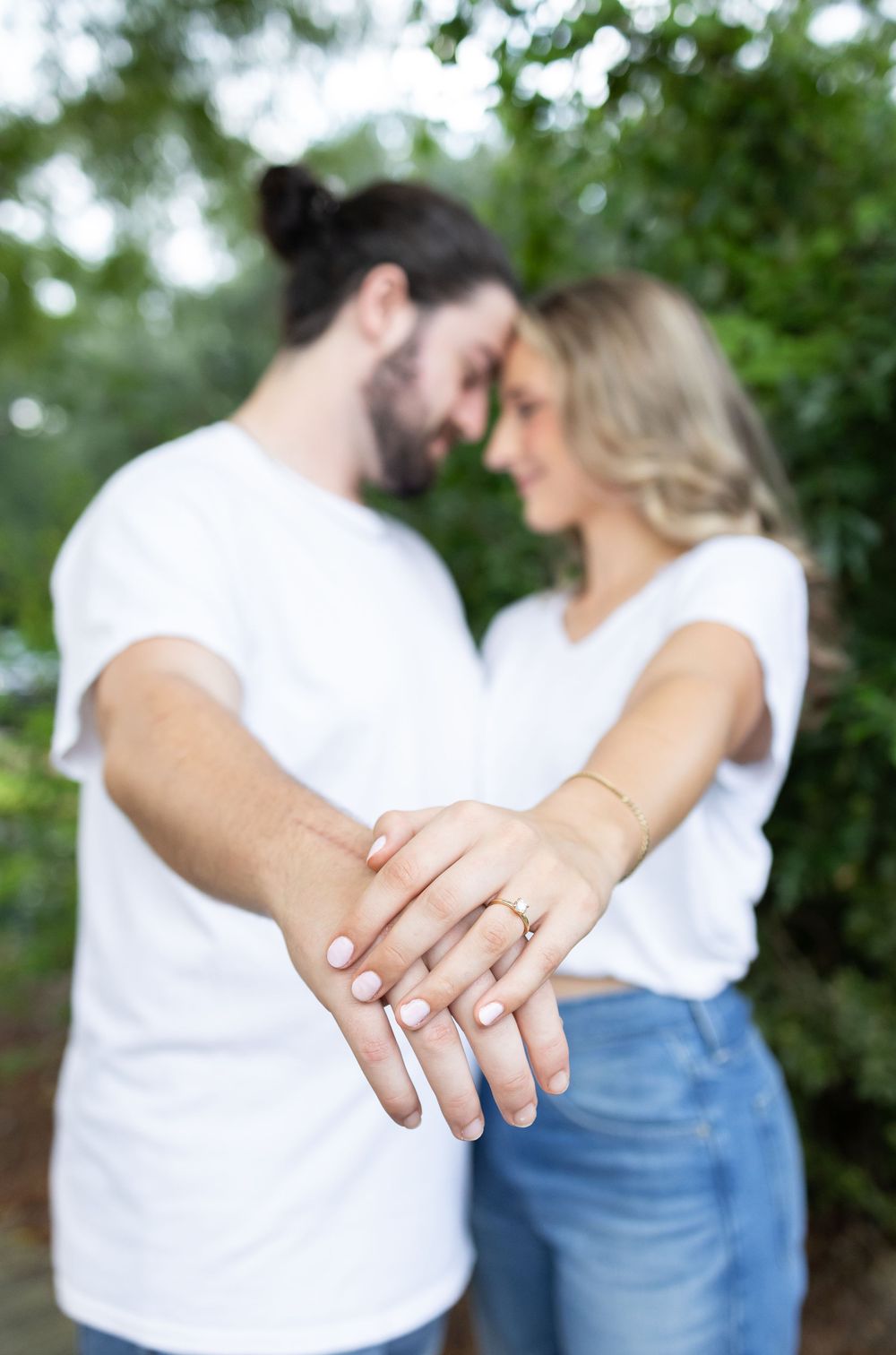 Engaged couple showing off ring while touching foreheads in romantic outdoor garden setting.