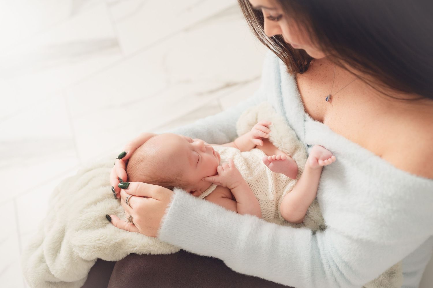 A mother tenderly cradles her sleeping newborn baby in her arms, wrapped in a soft white blanket.