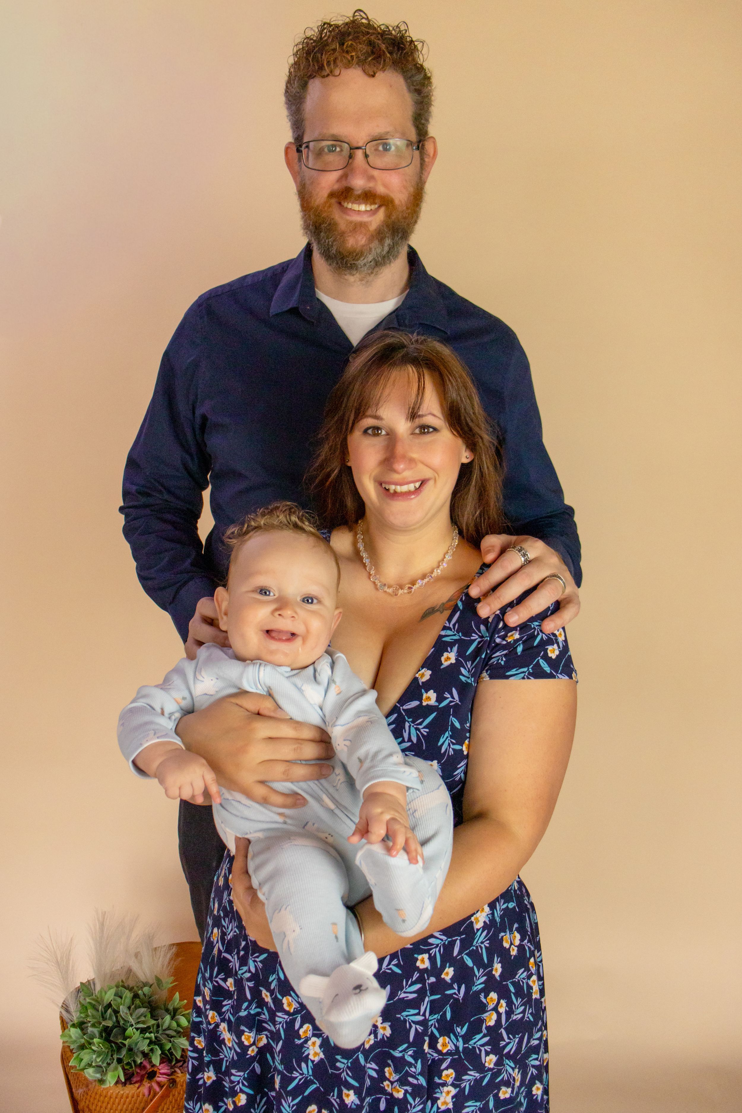 A smiling family portrait of a father, mother in floral dress, and happy baby in a studio setting with pierce county washington photographer