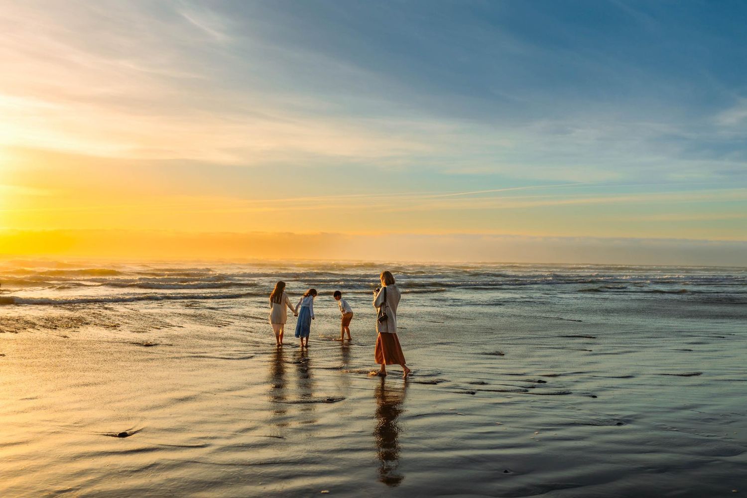 Family of four silhouetted against a vibrant sunset on a tranquil beach with golden reflections on wet sand.