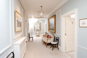 Elegant hallway with light blue walls, gold-framed mirrors, ornate chandelier, classic furniture, and white wainscoting.