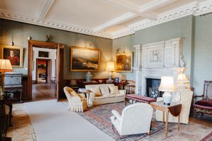 Elegant Georgian drawing room with ornate plasterwork, fireplace, oil paintings, and classic upholstered furniture on a Persian rug.