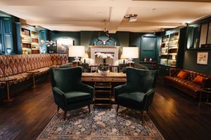 Sophisticated lounge with green velvet armchairs, tufted sofa, Persian rug, and built-in bookshelves in warm lighting.