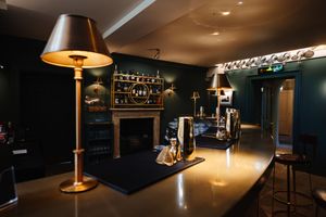 Elegant dimly lit bar interior with gold lamp, dark green walls, fireplace, and polished counter in a luxury venue.