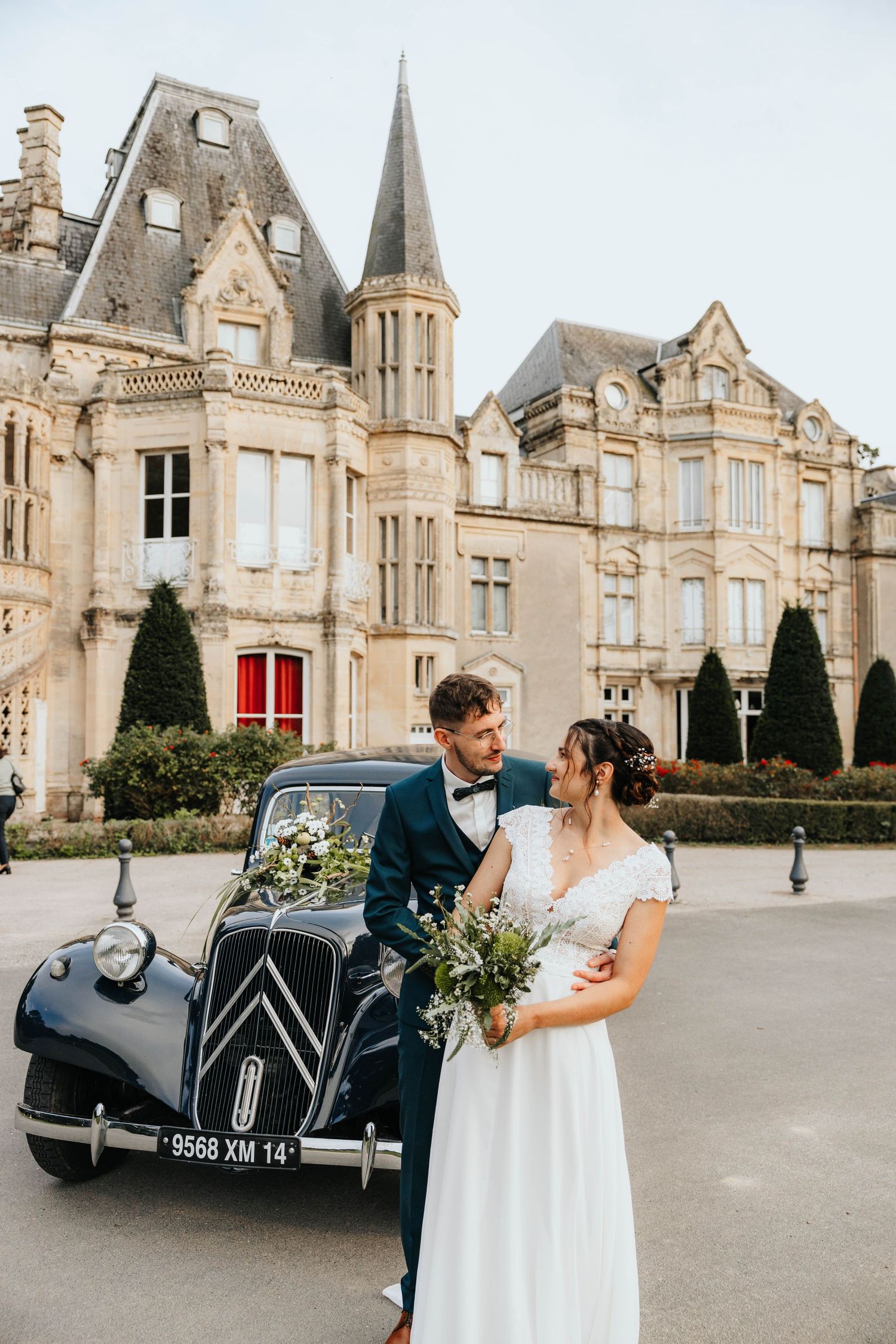 Bride and groom pose with wedding party outdoors on green lawn near rustic wooden arch, celebrating joyfully.