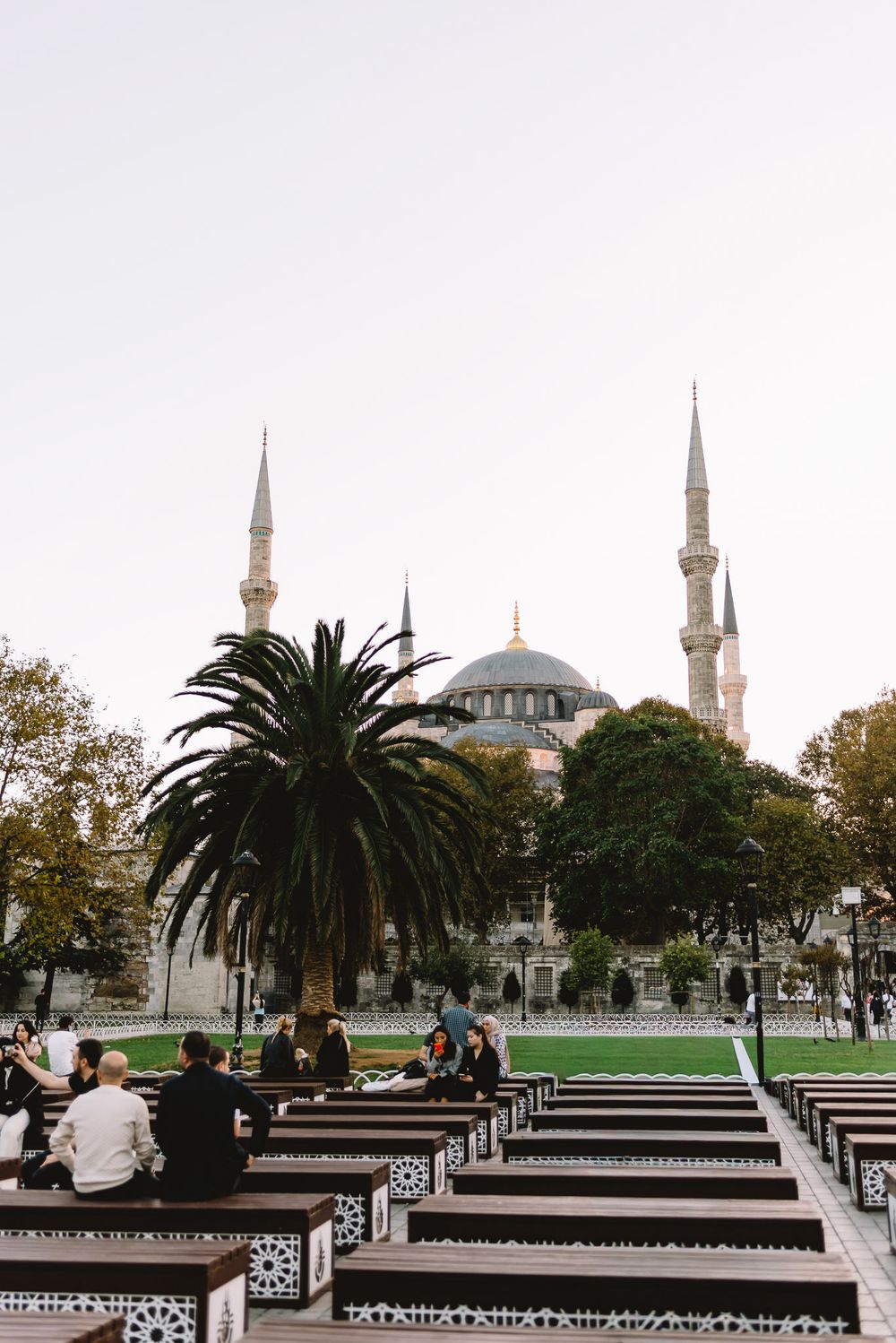 People sitting on ornate benches in Sultanahmet Square with the iconic Blue Mosque and minarets in Istanbul, Turkey.