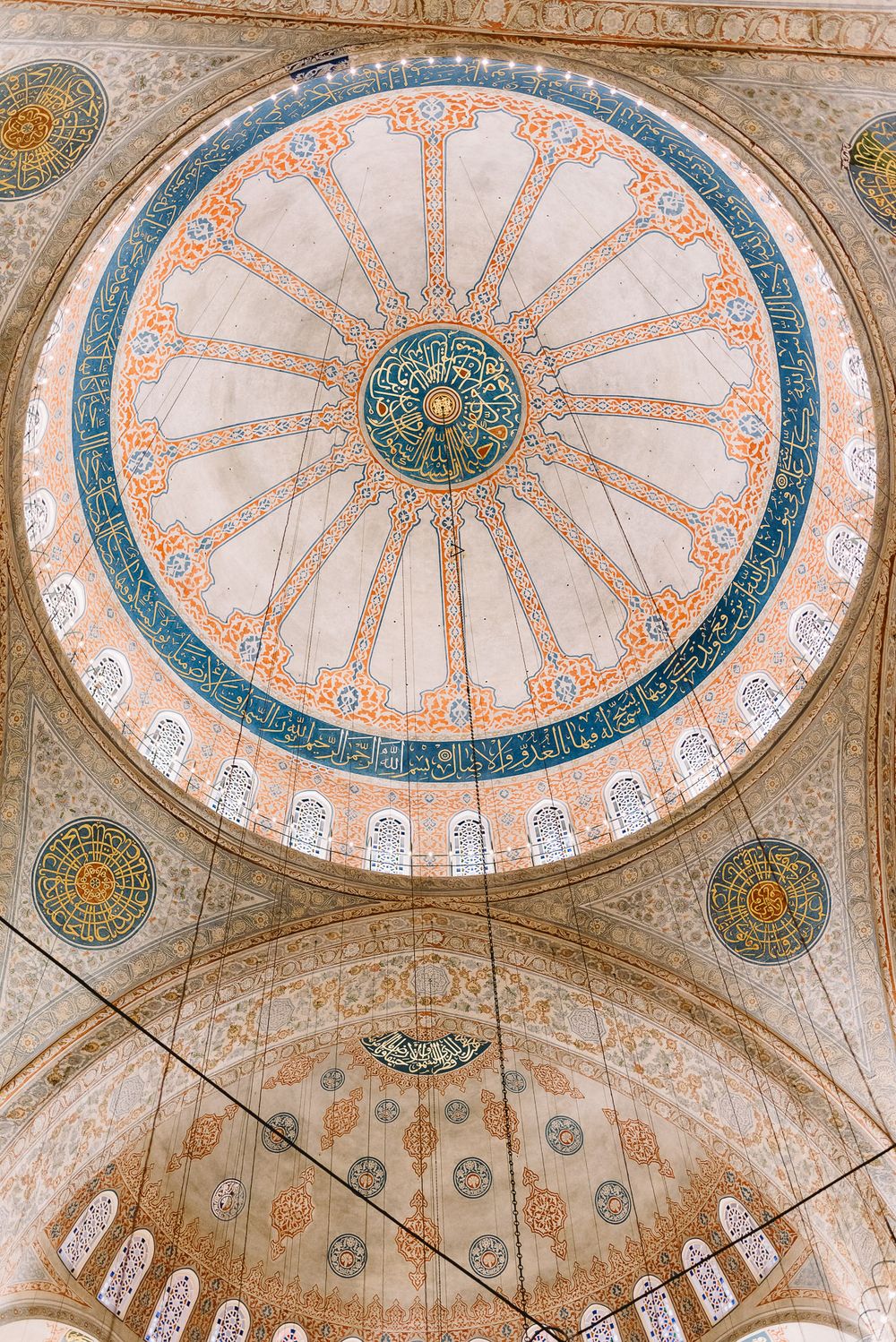 Ornate interior dome of the Blue Mosque in Istanbul, featuring intricate Islamic geometric patterns in blue, orange, and gold.