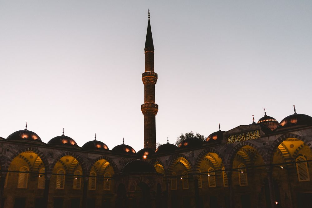 Illuminated domes and minaret of a historic mosque silhouetted against a twilight sky in Istanbul, Turkey.