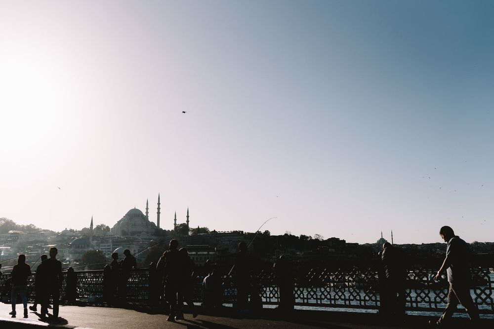 Silhouettes of people on Galata Bridge with the Blue Mosque skyline and Golden Horn in Istanbul, Turkey.
