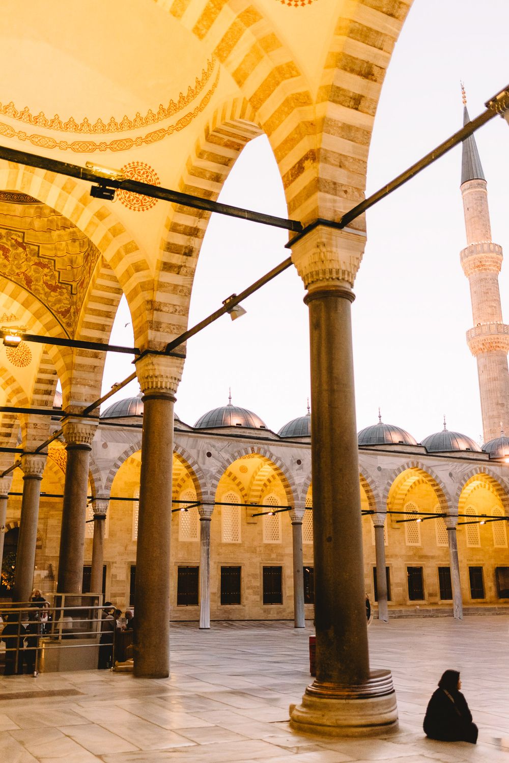 A person in black robes sits in the ornate courtyard of the Blue Mosque in Istanbul, Turkey.