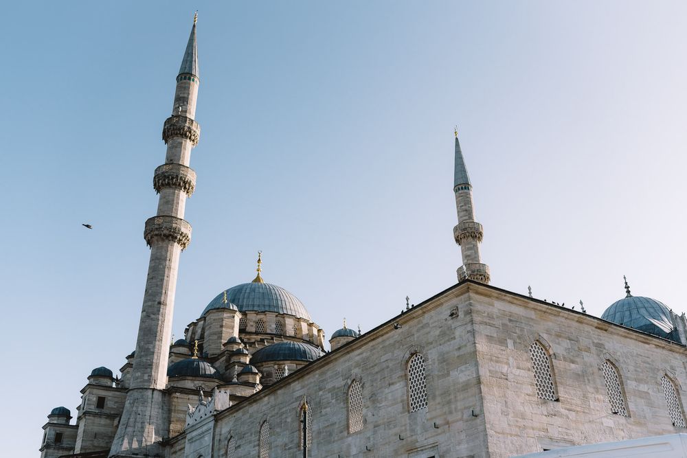 Stunning low-angle view of a historic Ottoman mosque with tall minarets and blue domes against a clear sky.
