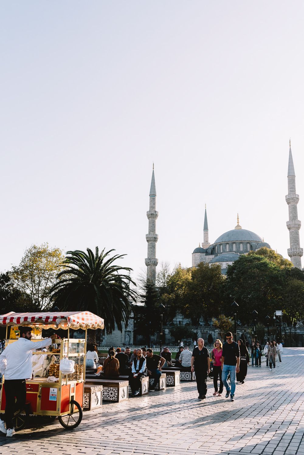 Tourists walk near a street food cart with the iconic Blue Mosque and its six minarets in Istanbul, Turkey.